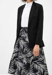 Černý blazer přes bílou plisovanou blůzu, doplněný sukní s černo-bílým vzorem palmových listů. Hladké textury a vypasovaný střih.