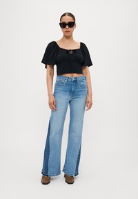 Svart kort topp med pufferm og knytedetalj foran, parret med lyseblå, vide jeans med kontrasterende sidestoff. Brune hæler.