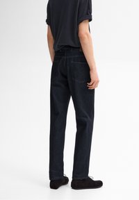 Mörkblå denimjeans med en avslappnad passform, fem fickor och subtila sömnadsdetaljer. Kombineras med en svart t-shirt med uppvikt ärm och mörka skor.