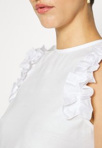 Biała bawełniana bluzka z falbankami na ramionach, gładkim, dopasowanym fasonem i okrągłym dekoltem.