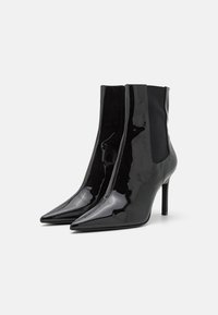 Černé kotníkové boty z lakované kůže se špičatou špičkou, vysokými jehlovými podpatky a elastickými bočními panely pro snadné nazouvání. Hladký lesklý povrch.