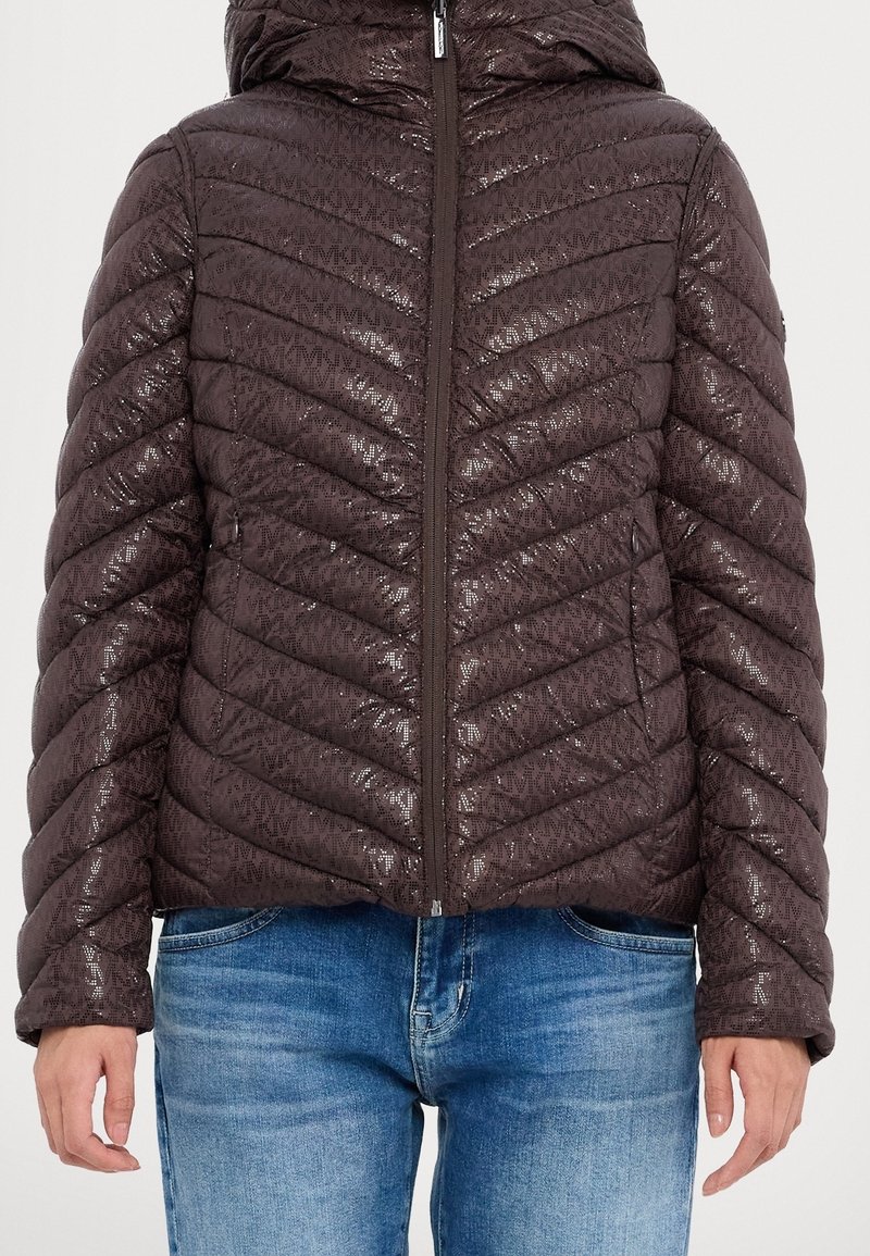 Veste matelassée brune avec une texture brillante, capuche et fermeture éclair. Présente un motif en chevrons et des poches latérales, assortie à un jean bleu.