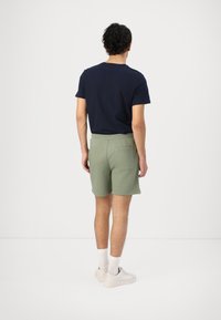 T-shirt bleu marine à manches courtes, assorti à un short en coton vert avec une taille élastique et une poche arrière. Chaussettes blanches et baskets.