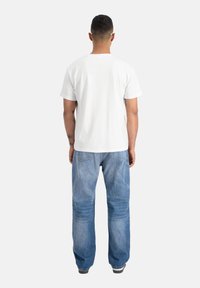 Tricou alb din bumbac cu guler rotund, asociat cu blugi din denim albastru deschis cu o croială relaxată și cusături vizibile pe buzunarele din spate.