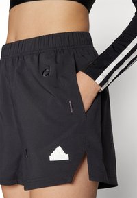 Svarta träningsshorts med resårmidja, sidofickor och en vit Adidas-logotyp nära fållen. Har små sprund på sidorna.