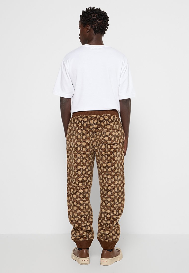 Brązowe dżinsy z wzorem o miękkiej fakturze, z elastycznymi mankietami i gumką w pasie. Połączone z gładką białą koszulką z krótkim rękawem.