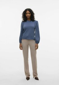 Maglia blu a maniche lunghe con scollo rotondo, abbinata a pantaloni beige attillati e tacchi a punta marroni, con hardware decorativo.
