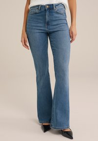 Uppvikta jeans i medelblå denim. Hög midja med fem fickor, en metallknapp och subtila sömnadsdetaljer. Raka ben som fladdrar.
