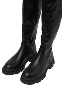 Stivali neri in pelle al ginocchio con una texture liscia, zip laterale e suole in gomma chunky. Presentano una punta arrotondata e una silhouette aderente.