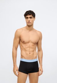 Juodi bokseriai su šviesiai mėlynu diržo kraštu su užrašu "Calvin Klein". Sklandaus audinio, prigludęs dizainas ir trumpa ilgis.