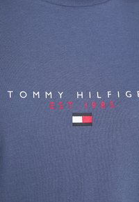Námořnická modrá bavlněná tričko s bílým textem "TOMMY HILFIGER", červeným "EST. 1985" a malým logem s červenými, bílými a černými akcenty.