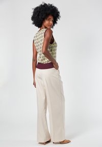 Top senza maniche lavorato a maglia con motivo geometrico verde e viola, abbinato a pantaloni a gamba larga color crema. Include un dettaglio testurizzato in vita.