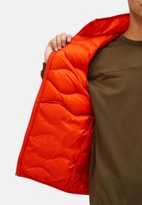 Giacca imbottita con fodera interna arancione brillante, che presenta un motivo a trapunta. Strato esterno di colore verde oliva con una superficie testurizzata. Chiusura con zip.