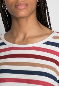 Haut en tricot rayé avec des lignes horizontales rouges, roses, bleues et beiges sur un fond blanc. Encolure arrondie et tissu texturé.