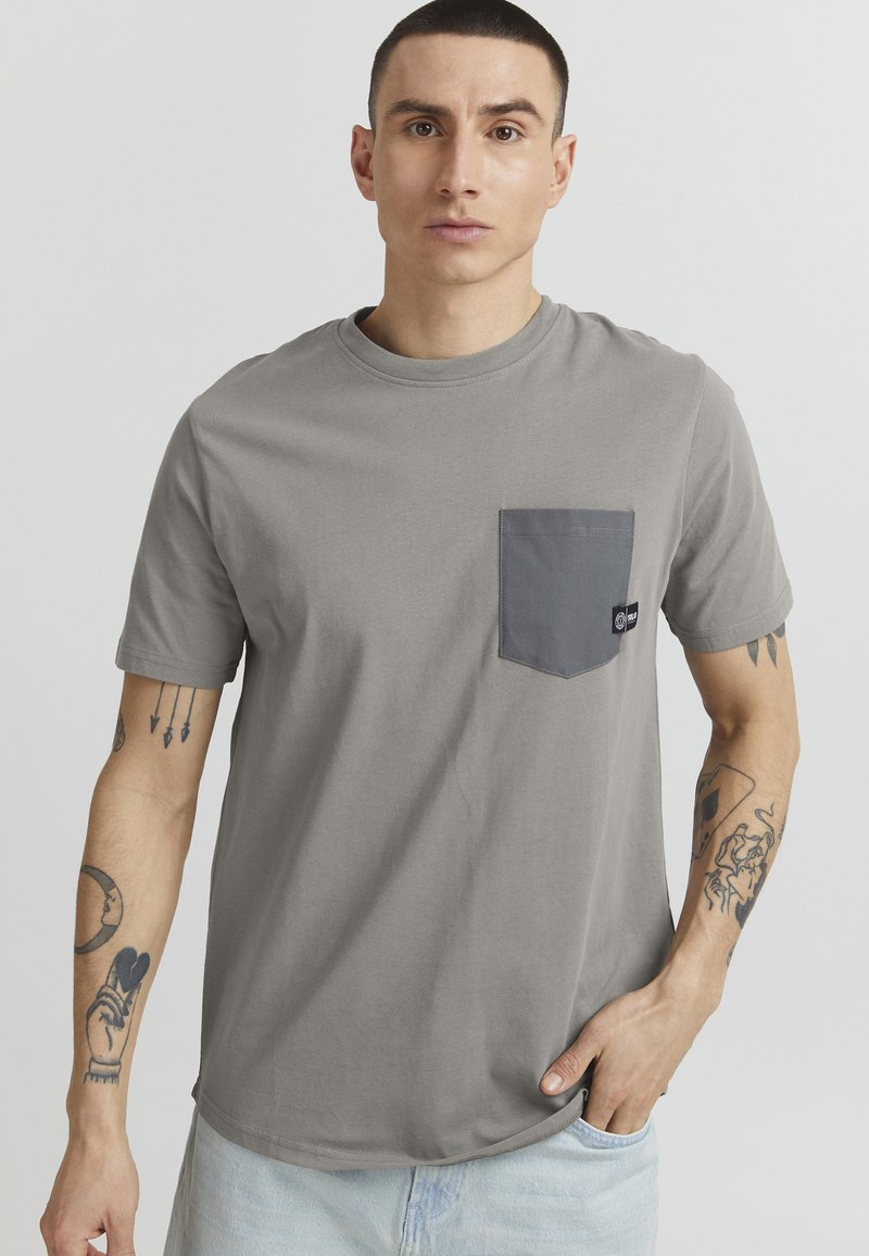 Gray short-sleeve t-shirt in soft cotton with a contrasting dark gray chest pocket and a logo tag on the pocket. Smooth texture, relaxed fit.