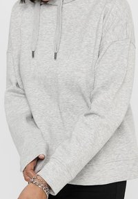 Hoodie grigio chiaro realizzato in tessuto morbido, dotato di cappuccio con stringa, vestibilità ampia e polsini a costine, con una texture liscia e senza fantasie.