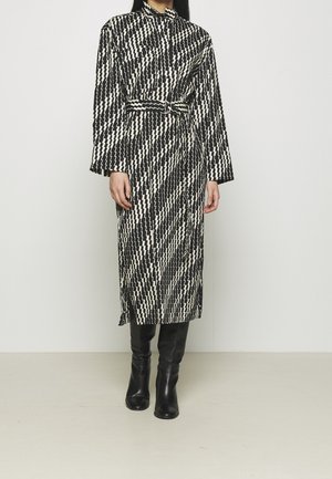 Kobieta ubrana w długą sukienkę w czarno-biały wzór zygzaka z paskiem, w połączeniu z czarnymi skórzanymi kozakami do kolan.