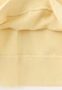 Gros plan d'un tissu tricoté beige avec différents points de tricot et un ourlet côtelé.