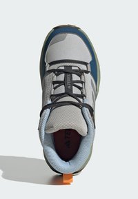 Šedá a modrá sportovní obuv s prodyšným síťovaným svrškem, černými tkaničkami, oranžovou záložkou na patě a texturovanou gumovou podrážkou s výztuhami.