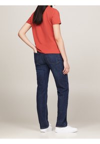 Rød kortærmet T-shirt parret med mørkeblå slim-fit jeans og hvide sneakers, der viser en glat tekstur og klassisk design.