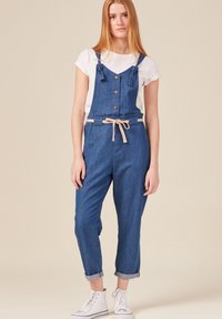 Ogrodniczki denimowe z regulowanymi ramiączkami, frontowymi guzikami i związanym paskiem w kontrastowym kolorze. Rolowane mankiety i boczne kieszenie dopełniają całość.