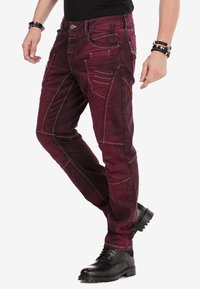 Bordeaux jeans met contrasterende stiksels, slim fit, meerdere zakken en een gestructureerde afwerking, gecombineerd met zwarte boots.