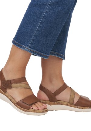 Brown leather sandals with cork soles. Features cross-straps and a Velcro closure. Light tan accents; low wedge heel. Casual design.