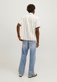 Chemise à manches courtes de couleur claire avec des rayures, fabriquée dans un tissu texturé, associée à un jean bleu clair. Coupe décontractée avec un design relax.