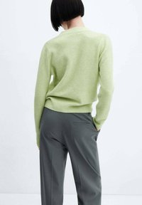 Světle zelený svetr s jemnou texturou, kulatým výstřihem a žebrovanými manžetami, v kombinaci s šedými kalhotami na míru s zadní kapsou.