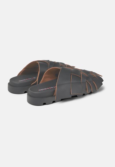 Zwarte instapsandalen met gevlochten banden, met een gestructureerd oppervlak en contrasterende bruine accenten. Platte zool met een ronde neus.