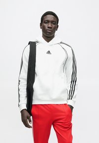Biela mikina s čiernymi pruhmi na rukávoch, ktorá má malý čierny logo. Kombinovaná s jasne červenými nohavicami s voľným strihom.