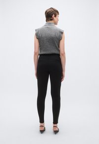 Top gri fără mâneci cu guler înalt și textură striată, asortat cu colanți negri mulati și pantofi negri cu toc înalt, văzut din spate.