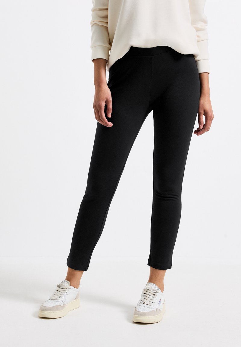 Leggings neri aderenti in un tessuto liscio ed elasticizzato, dotati di una vita alta e un design elegante. Abbinati a sneakers bianche.