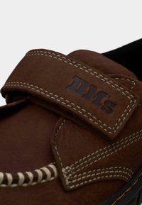 Καφέ δερμάτινο παπούτσι με λευκή ραφή και λουράκι με βέλκρο που φέρει ανάγλυφα γράμματα "DMS".