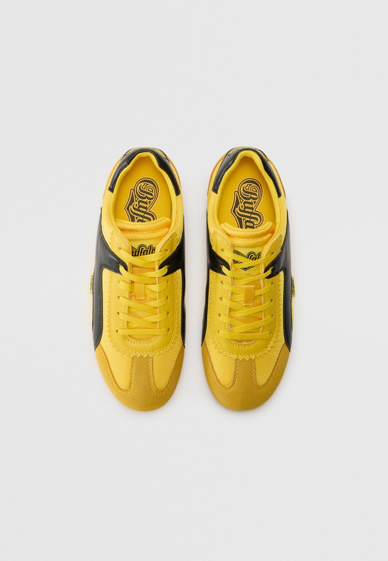 Zapatillas amarillas y negras con un upper de tejido texturizado, punta redonda y detalles en negro, con cordones planos y una lengua acolchada para mayor confort.