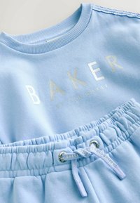 Gaiši zils džemperis ar metāliskā sudraba "BAKER" tekstu, ar ribotu apkakli un saskaņotas sporta bikses ar elastīgu jostu un auklu.