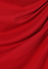 Tissu rouge à texture lisse, présentant un tombé et des plis délicats, mettant en valeur une couleur riche et uniforme ainsi qu'un éclat doux.