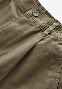 Olivgrüne Baumwollhose mit elastischem Bund, Knopfverschluss und seitlicher Tasche. Glatte Textur mit sichtbaren Nähdetails.