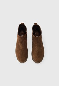 Botas de tobillo de ante marrón con una textura suave, punta redondeada, inserciones elásticas a los lados y una lengüeta en la parte trasera para facilitar el calzado.