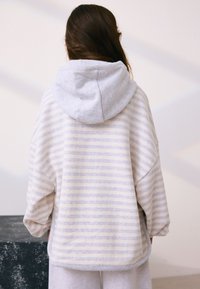 Bluza pulover cu dungi în crem și gri deschis, cu croială lejeră și glugă gri. Țesătură moale cu manșete și tiv rib.