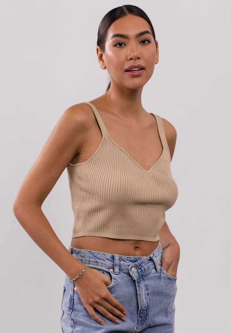 Beige geripptes Crop-Top mit V-Ausschnitt, dünnen Trägern und tailliertem Schnitt, kombiniert mit hellblauen, hochgeschnittenen Jeansshorts.