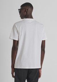Camiseta blanca de manga corta, cuello redondo, fabricada en algodón suave, corte regular. Sin patrones, diseño sencillo, vista trasera que muestra una textura y bordes suaves.