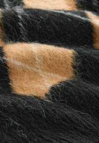 Tissu en laine présentant un motif à carreaux avec des carrés alternés noirs et orange clair. Surface texturée avec de fines fibres et un léger brillant.