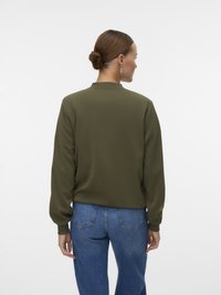 Haut à manches longues vert olive avec un col rond et des poignets côtelés, associé à un jean en denim bleu. Couleur unie, texture lisse.