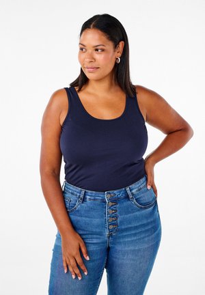 Top corto navy de tela suave, con escote redondeado y tirantes anchos, combinado con jeans de mezclilla de cintura alta con detalles de botones visibles.