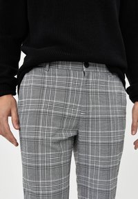 Šedé kostkované kalhoty s mixem černých a bílých pruhů. Mají dva boční kapsy a design s poutky na opasek. Nosené s černým pleteným svetrem.