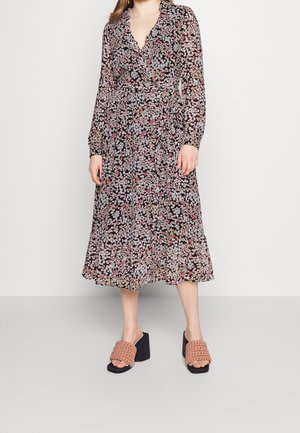 Robe portefeuille florale à manches longues, fond noir, fleurs pink et blanches dispersées, et ourlet ondulé. Assortie à des talons à enfiler tissés beiges.