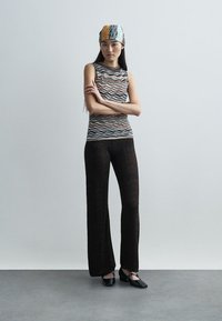 Πλεκτό αμάνικο τοπ με κυματιστά μοτίβα σε γήινες αποχρώσεις, συνδυασμένο με μαύρο φαρδύ παντελόνι με ανάγλυφη σχεδίαση ζιγκ-ζαγκ και επίπεδες γόβες.