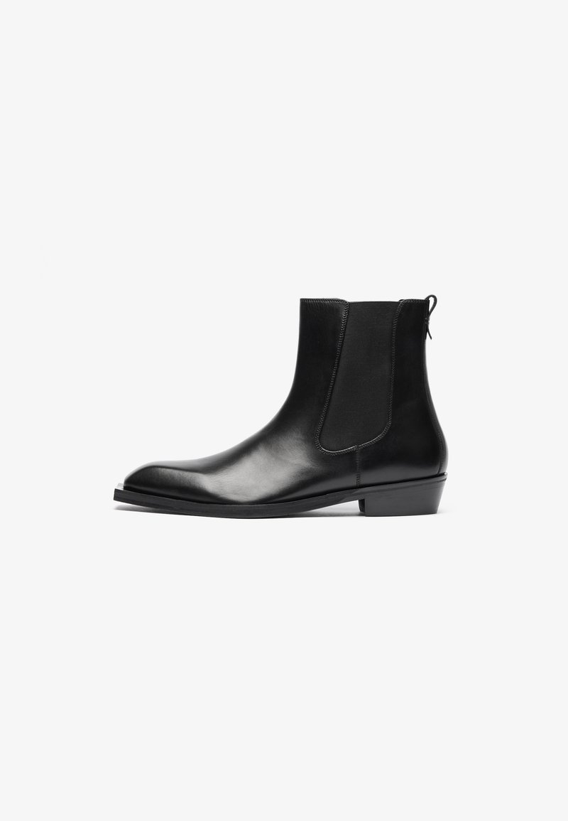 Bottines noires en cuir avec des panneaux élastiques sur les côtés, bout rond et petit talon carré. Texture lisse avec un design minimaliste.