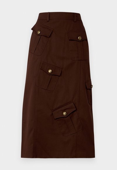 Brūns ceļgala garuma svārki, izgatavoti no kokvilnas, ar vairākiem kabatām ar atlokiem, kas rotāti ar zelta pogām un pieguļošu jostu. Gluda tekstūra.